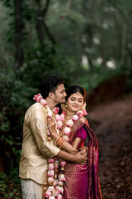 Traditional Sri Lankan wedding portrait by Udayaa Studio — bride and groom in floral garlands in a lush green outdoor setting