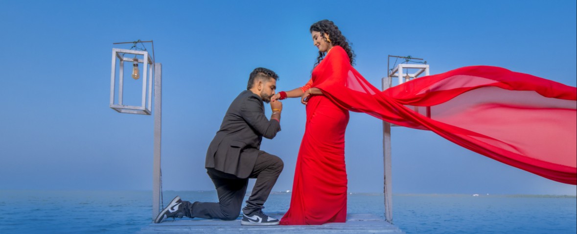 Romantic pre-wedding shoot by Udayaa Studio — couple on an ocean jetty, scarlet saree flowing in the sea breeze